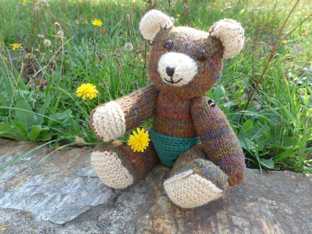 Strickteddy mit grüner Hose sitzt auf einer Mauer